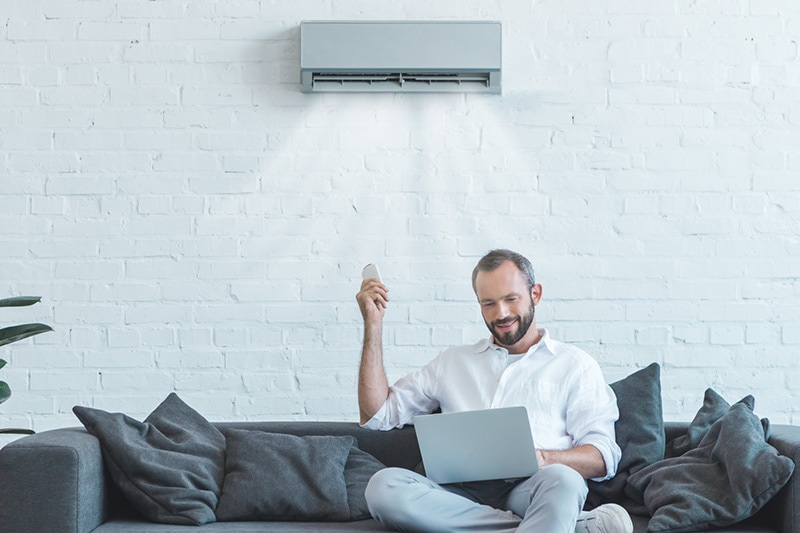 man using remote control to turn on ductless unit from his couch.