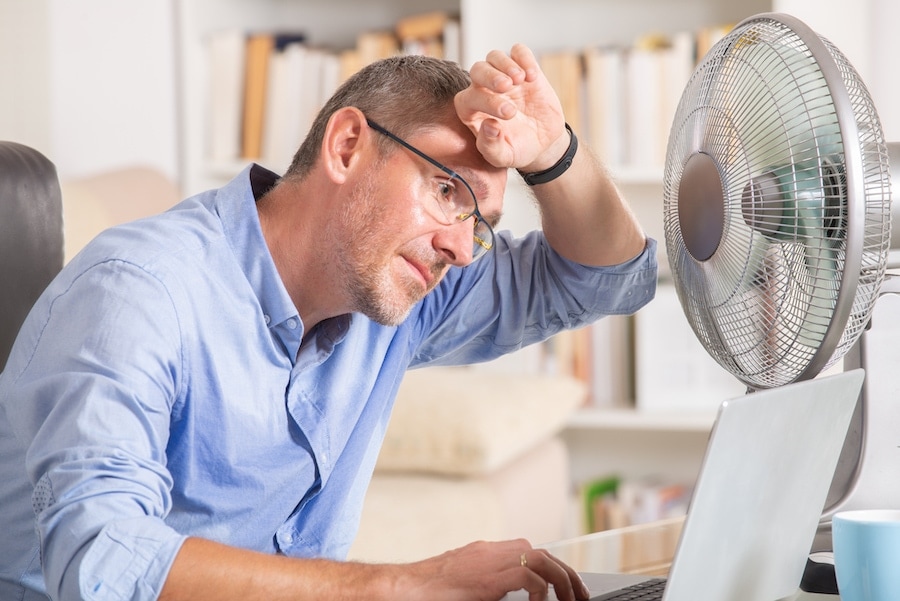 Is your heat pump blowing warm air on a hot day? Man suffers from heat while working in the office and tries to cool off by the fan.
