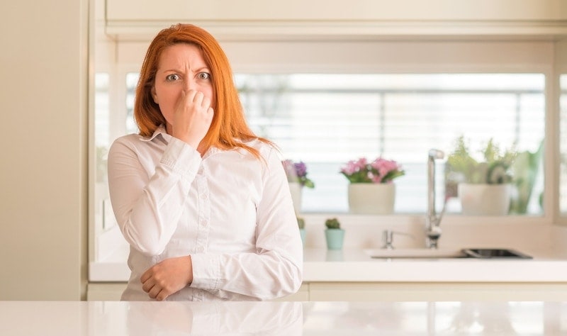 A woman in her kitchen plugging her nose because her furnace smells strange.