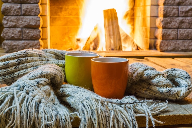factors to consider when buying a heat pump. A comfy scene with mugs and coffee and a fireplace.